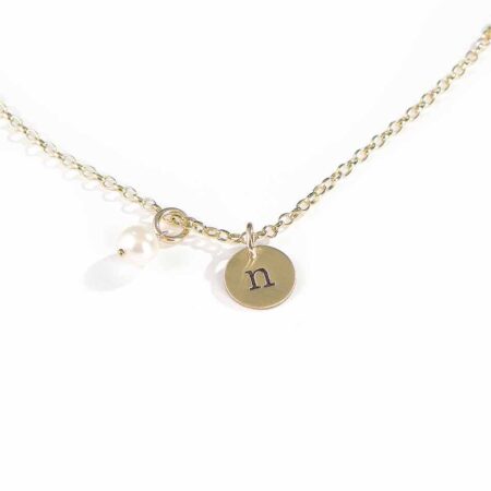 A personalized jewelry piece with hand stamped initial on the dainty gold-filled disc