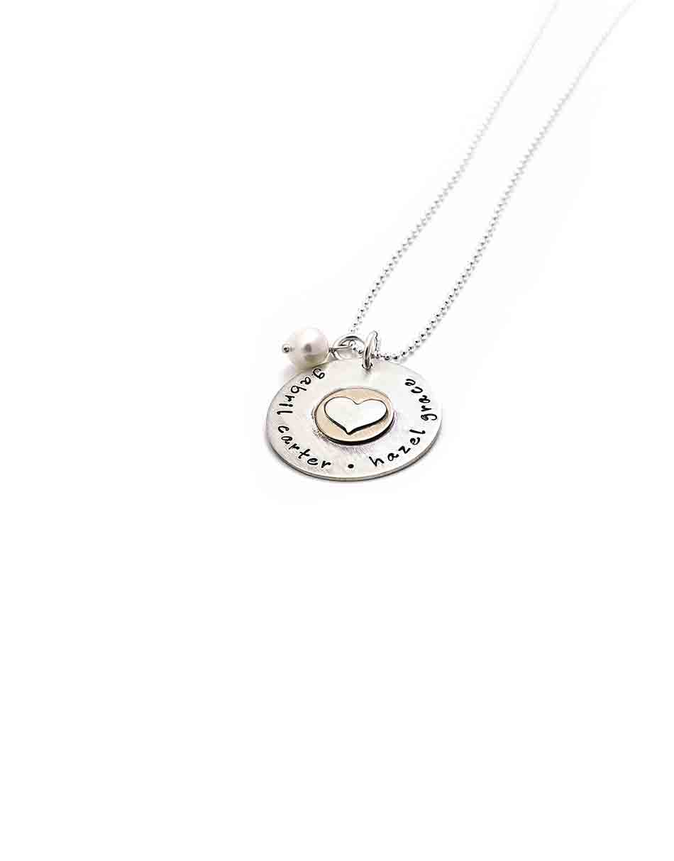 A sterling silver disc with hand stamped names. Layered with a gold-filled disc and a sterling silver heart in the middle.