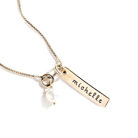 A beautiful gold-filled charm hand stamped with name. Hung on a gold-filled chain with a freshwater pearl.